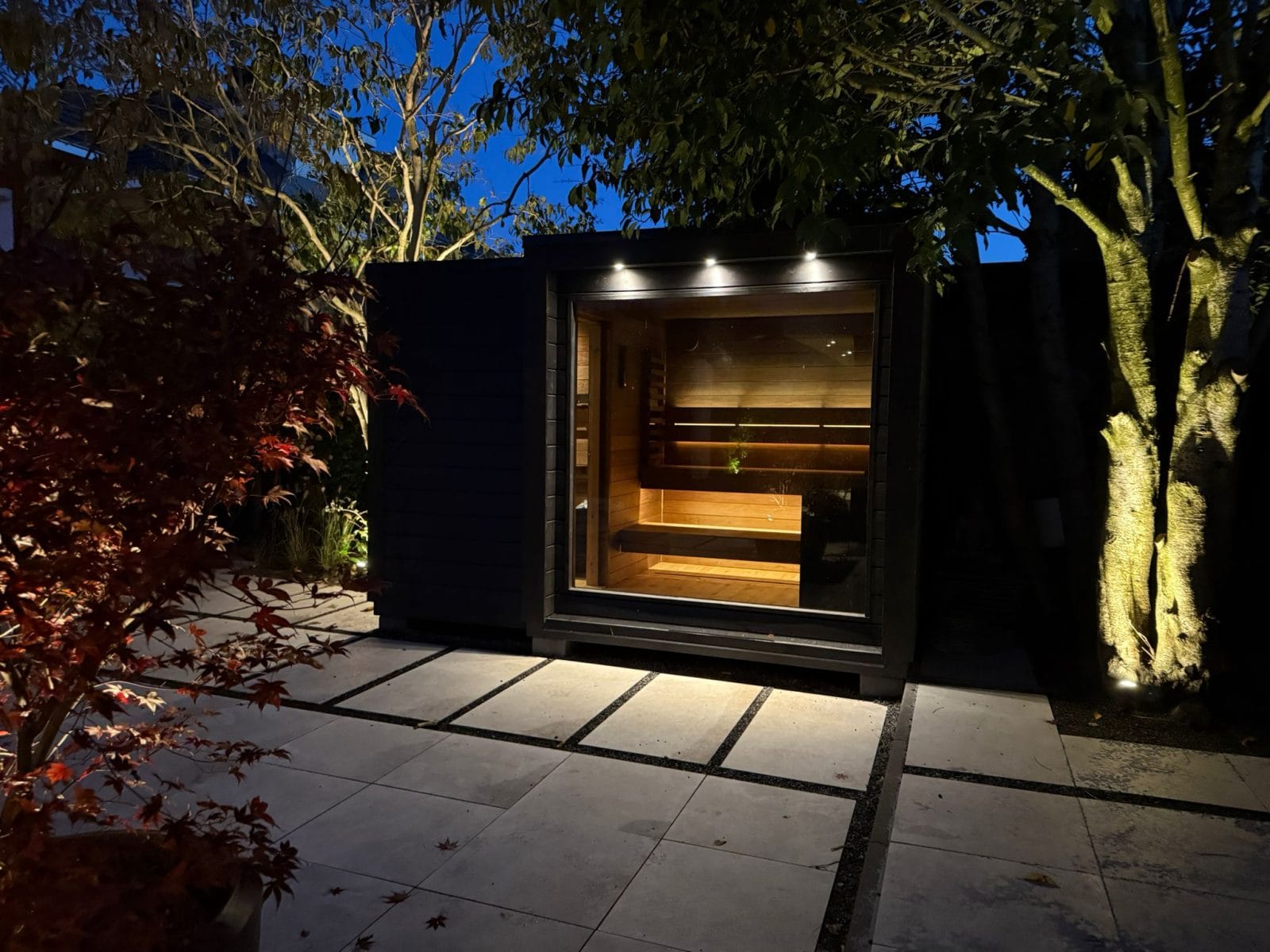 Mökki buitensauna in het donker met sfeerverlichting, warm verlichte ramen en een luxe wellnessuitstraling in de tuin.